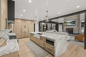 Kitchen with light brown cabinetry, light wood-style flooring, a large island with sink, light stone countertops, and recessed lighting