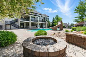 Rear view of property with an outdoor fire pit, a balcony, an outdoor pool, a patio, and stairs