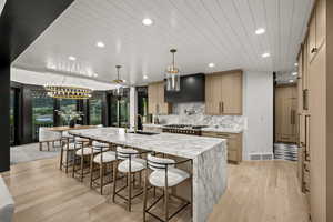Kitchen with custom range hood, recessed lighting, light wood-type flooring, a spacious island, and backsplash