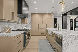 Kitchen featuring wall chimney exhaust hood, double oven range, light brown cabinets, recessed lighting, and stainless steel microwave