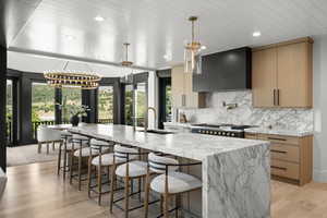 Kitchen featuring wall chimney exhaust hood, a chandelier, a large island, tasteful backsplash, and light wood finished floors
