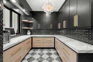Kitchen featuring open shelves, dark cabinetry, decorative backsplash, and light stone counters