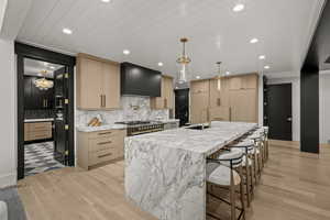 Kitchen featuring wall chimney range hood, light brown cabinets, light wood-style floors, tasteful backsplash, and recessed lighting