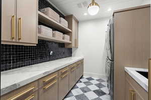Kitchen with open shelves, estacked washer and dryer, tasteful backsplash, light flooring, and light stone counters