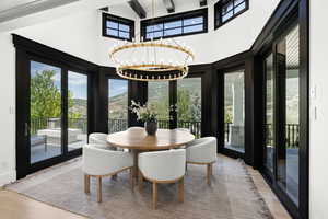 Dining room with french doors, a towering ceiling, wood finished floors, a chandelier, and beamed ceiling
