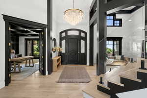 Foyer entrance featuring a chandelier, a towering ceiling, light wood-style floors, and healthy amount of natural light