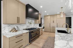 Kitchen featuring double oven range, wall chimney range hood, light brown cabinetry, light stone countertops, and recessed lighting
