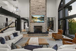 Living room featuring a high ceiling, a stone fireplace, wood finished floors, and stairs