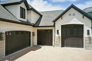 View of front facade with roof with shingles, decorative driveway, stone siding, and an attached garage
