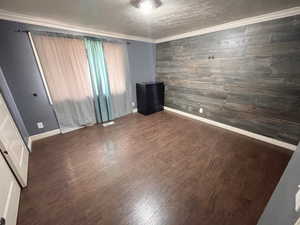 Main bedroom featuring wooden walls, wood finished floors, crown molding, and a textured ceiling