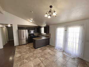 Kitchen featuring appliances with stainless steel finishes, vaulted ceiling, a peninsula, a textured ceiling, and a chandelier