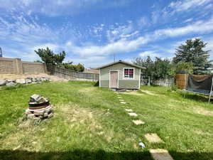 Fenced backyard featuring a trampoline and an outdoor structure