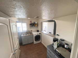 Downstairs Kitchen / Laundry room featuring washer. cabinet space, dark wood finished floors, arched walkways, and a textured ceiling