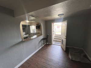 Dining room with a textured wall, arched walkways, dark wood finished floors, and a textured ceiling