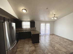 Kitchen featuring freestanding refrigerator, a peninsula, vaulted ceiling, tasteful backsplash, and a chandelier