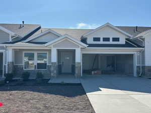 View of front facade with concrete driveway, stone siding, roof with shingles, and a garage