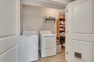 Laundry room with independent washer and dryer and light wood-style flooring