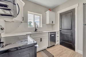 Kitchen with stainless steel dishwasher, electric stove, white microwave, tasteful backsplash, and white cabinetry