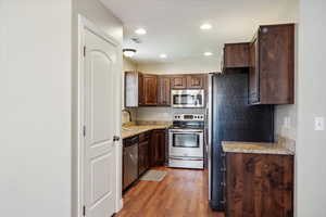 Kitchen featuring appliances with stainless steel finishes, wood finished floors, recessed lighting, dark brown cabinetry, and light stone countertops