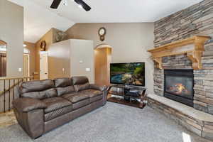 Carpeted living area with ceiling fan, lofted ceiling, a fireplace, and arched walkways