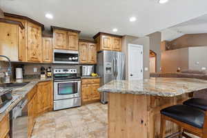 Kitchen featuring appliances with stainless steel finishes, a kitchen breakfast bar, light stone countertops, recessed lighting, and open floor plan