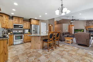 Kitchen featuring stainless steel appliances, open floor plan, light stone finish floors, recessed lighting, and vaulted ceiling