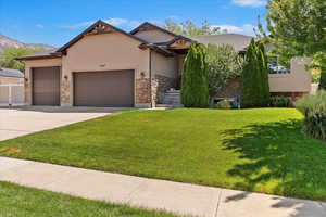 View of front of home with a garage, a front lawn, stucco siding, and stone siding