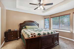 Bedroom with light colored carpet, a raised ceiling, and ceiling fan