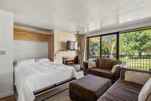 Bedroom with multiple windows, a lit fireplace, a textured ceiling, and access to exterior