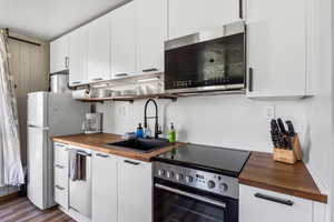 Kitchen featuring butcher block counters, appliances with stainless steel finishes, wood finished floors, and white cabinets