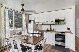 Kitchen with wood counters, stainless steel appliances, wood finished floors, white cabinetry, and a textured ceiling