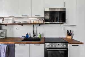Kitchen with butcher block counters, stainless steel appliances, open shelves, and white cabinetry