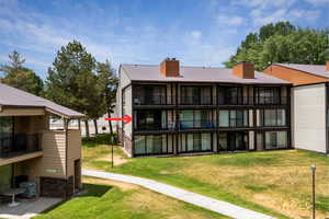 Back of house with a chimney, a balcony, a lawn, and stone siding