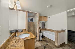 Full bath with a bath, vanity, a stall shower, and stone finish flooring