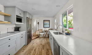 Kitchen featuring stainless steel appliances, light wood-style floors, light countertops, open shelves, and gray cabinetry