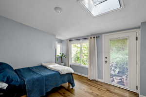 Bedroom with light wood-style flooring, lofted ceiling, a skylight, and access to outside