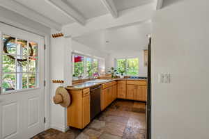 Kitchen featuring appliances with stainless steel finishes, beam ceiling, stone tile flooring, and light countertops