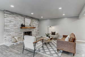 Living area featuring wood finished floors, recessed lighting, a brick fireplace, and crown molding