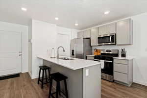 Kitchen with appliances with stainless steel finishes, gray cabinetry, a kitchen bar, dark wood-style flooring, and recessed lighting