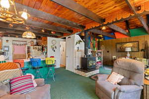 Carpeted living area featuring wood walls, a wooden ceiling with exposed beams, a wood stove, and a chandelier