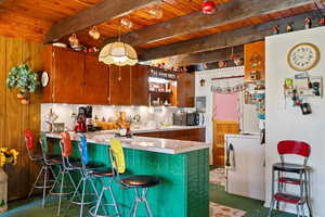 Kitchen with a peninsula, a wooden ceiling with exposed beams, dark carpet, light countertops, and a breakfast bar