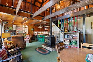 Dining space featuring a wood stove, carpet flooring, wooden walls, and a wood ceiling with exposed beams