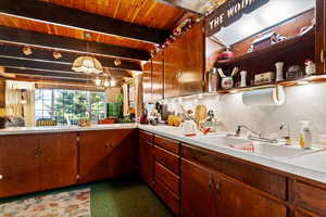 Kitchen with light countertops, a wooden ceiling with exposed beams, open shelves, and decorative light fixtures