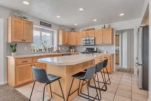 Kitchen with stainless steel appliances, a kitchen breakfast bar, light brown cabinetry, light countertops, and recessed lighting