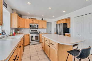 Kitchen featuring stainless steel appliances, a kitchen island, light tile patterned flooring, light countertops, and a kitchen bar