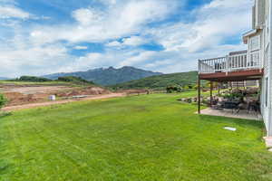 View of grassy yard with a patio and a deck with mountain view