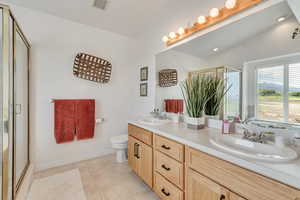 Full bath with a shower with door, double vanity, tile patterned flooring, and lofted ceiling