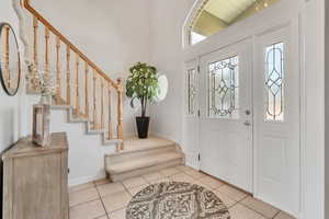 Entryway with healthy amount of natural light, stairs, tile patterned floors, and a high ceiling