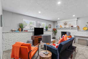 Carpeted living room with a brick fireplace, recessed lighting, and a textured ceiling
