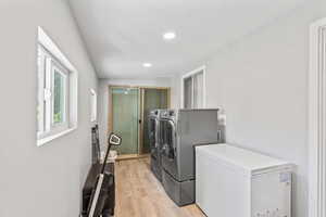 Laundry area with washer and dryer, light wood-type flooring, and recessed lighting